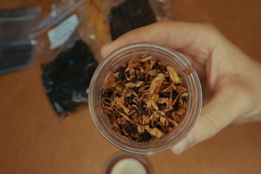 Mano che mantiene un barattolo di vetro pieno di tabacco da pipa su un tavolo.